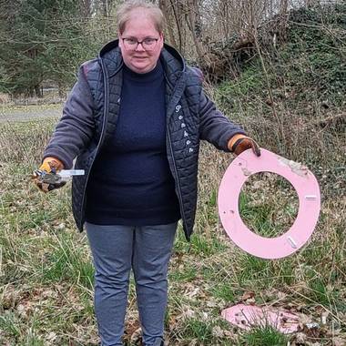 Eine Frau hat einen pinken Toilettendeckel und klein Müll in der Hand