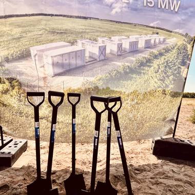 Mehrere Spaten stechen im Sand vor einem Transparent des Batteriespeichers