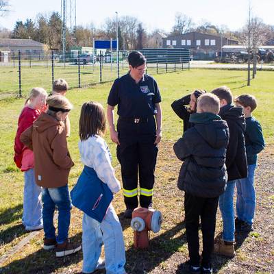 Frau Steinig-Pinnecke steht mit den Kindern an einem Hydranten auf dem Feuerwehrgelände