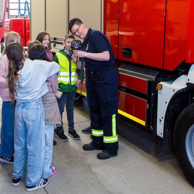 Frau Steinig-Pinnecke zeigt den Kindern wie die Wärmebildkamera funktioniert. Im Hintergrund stehen Fahrzeuge der Feuerwehr.