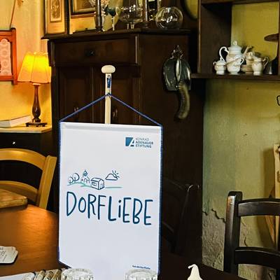 Es wird ein Raum gezeigt, dort sieht man einen Tisch mit Gläsern und Kerze darauf steht der Wimpel