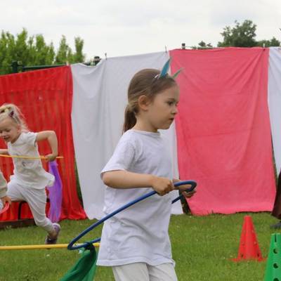 Drei Kinder mit Hula hoop Reifen um die Hüften laufen einen ausgezeichneten Rundkurs ab, ebenso beim Laufen ist eine Erzieherin zu sehen.