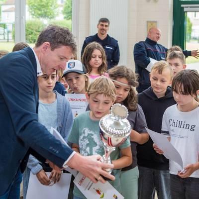 Bürgermeister überreicht Pokal und die Urkunden an die Kinder, die sich den Pokal anschauen.