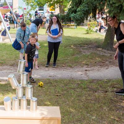 Ein Junge wirft einen Ball auf einen Stapel Büchsen, er trifft und ein paar Büchsen fallen herunter