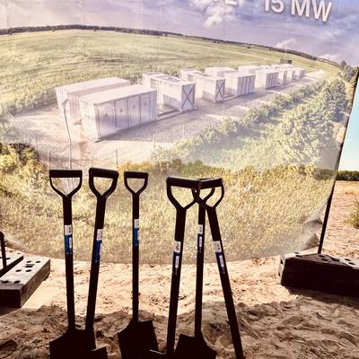 Mehrere Spaten stechen im Sand vor einem Transparent des Batteriespeichers