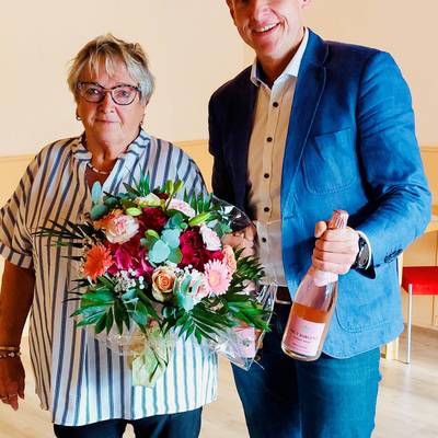 Herr Brohm gratuliert Frau Fischer zum 30-jährigen Jubiläum im Dienst der Dorfgemeinschaft mit einem Blumenstrauß und einer Flasche Sekt