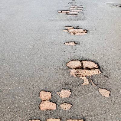 Zu sehen ist ein schadhafter Straßenbelag, bei welchem das darunterliegende Kopfsteinpflaster zu sehen ist